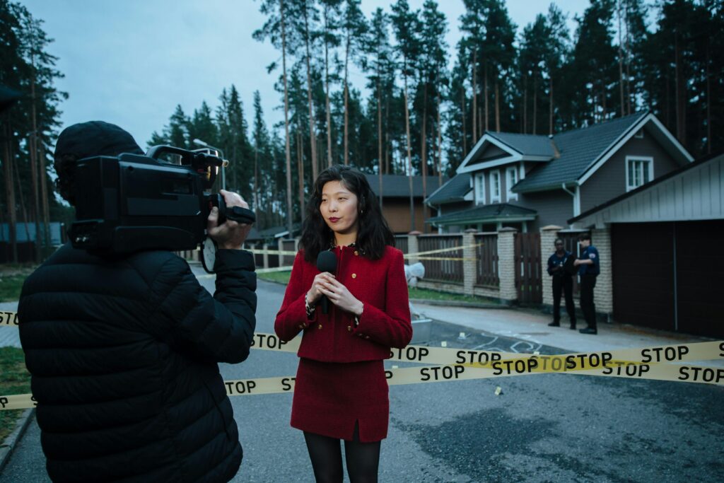 Journalist reporting live from a taped crime scene with cameraman and police.